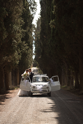 # The just married couple across a cypress boulevard with an old original FIAT 500.
